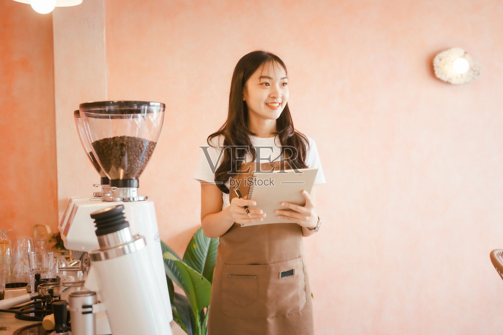 一位美丽的年轻女咖啡师在舒适的咖啡馆中微笑着制作新鲜咖啡，营造出温馨的氛围，熟练而迷人地为顾客服务。照片摄影图片