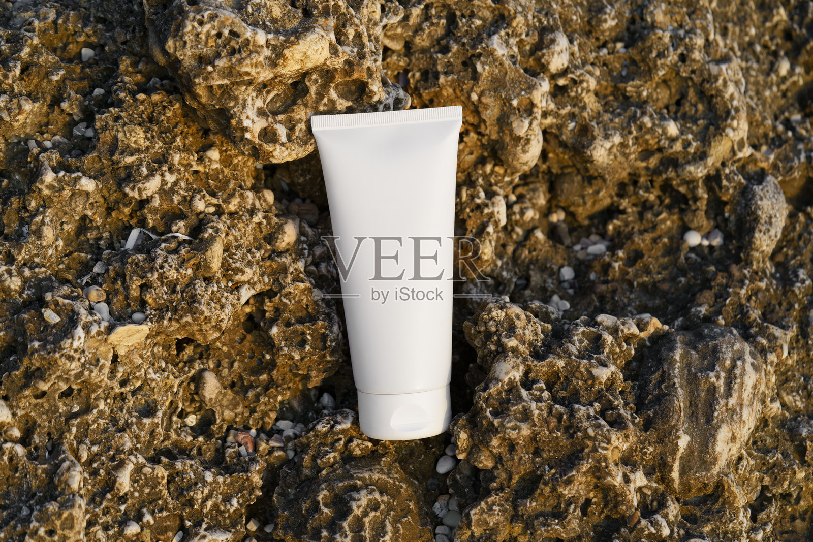 海滩上岩石旁的白色乳胶管装护肤霜。自然美容产品、面部和身体护理、防晒霜及防晒保护的概念。照片摄影图片