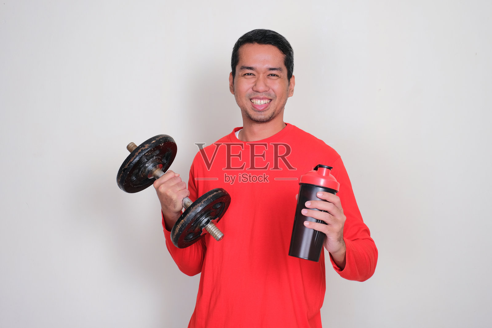 一个运动型男子微笑着，手里拿着哑铃和饮料杯。照片摄影图片