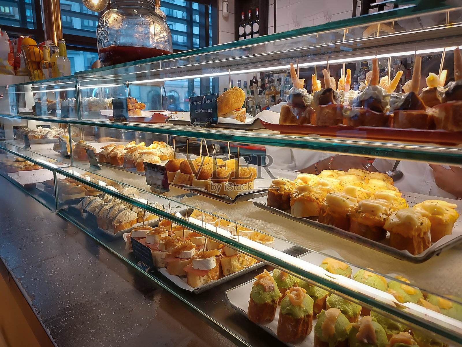 一个有三层展示柜的酒吧，展示各种典型的西班牙小吃和拼盘。照片摄影图片