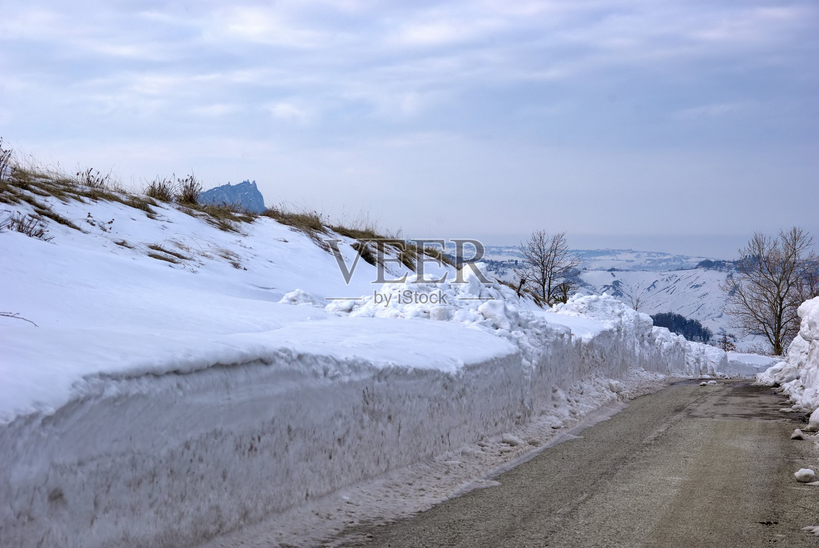 冰雪覆盖的道路在高高的雪堆中，映衬着阴 cloudy 的天空照片摄影图片