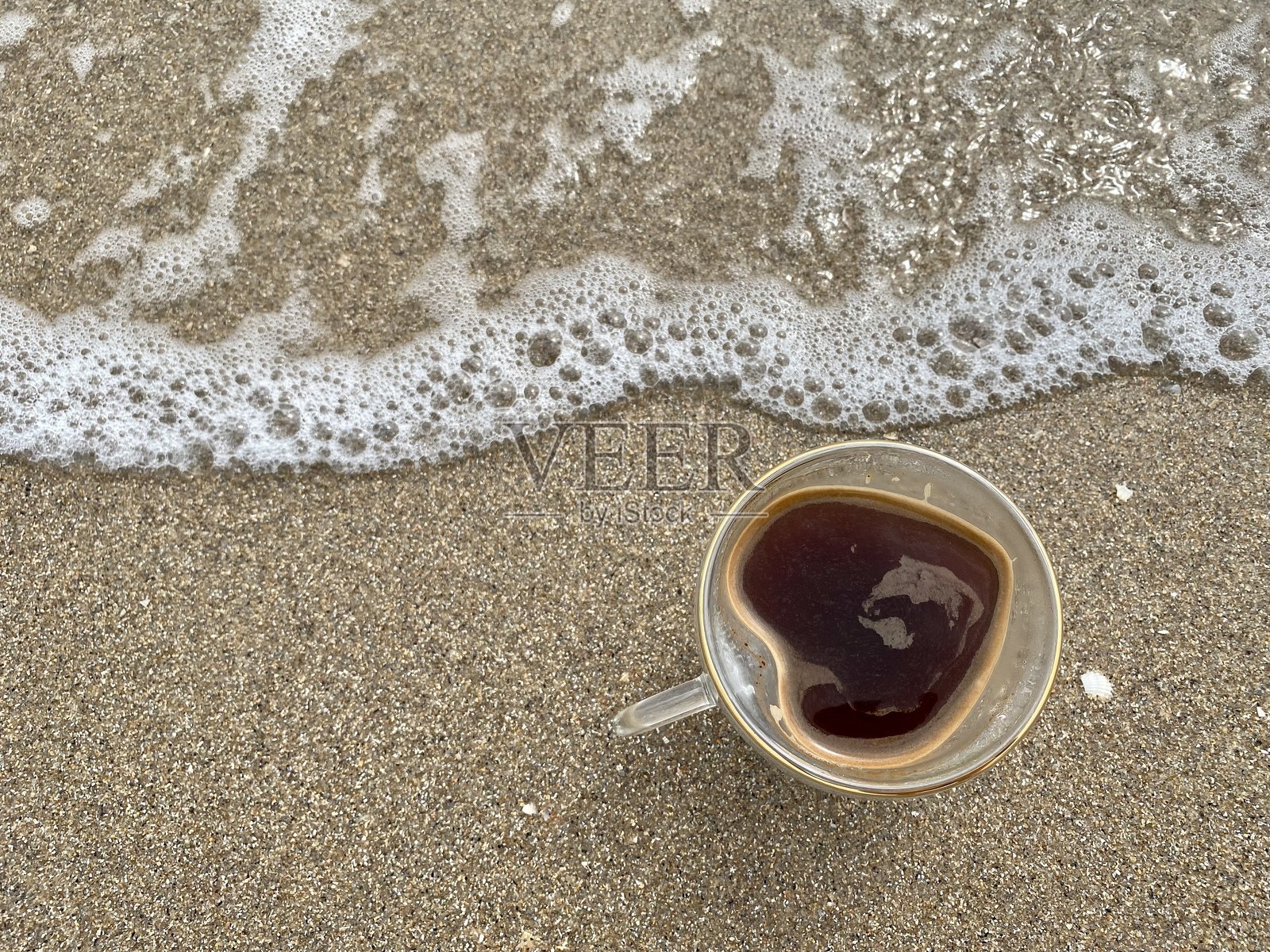 一个不寻常的心形咖啡杯静静地放在海边的沙滩上，完美的爱情夏季概念，度假或旅行社概念。照片摄影图片