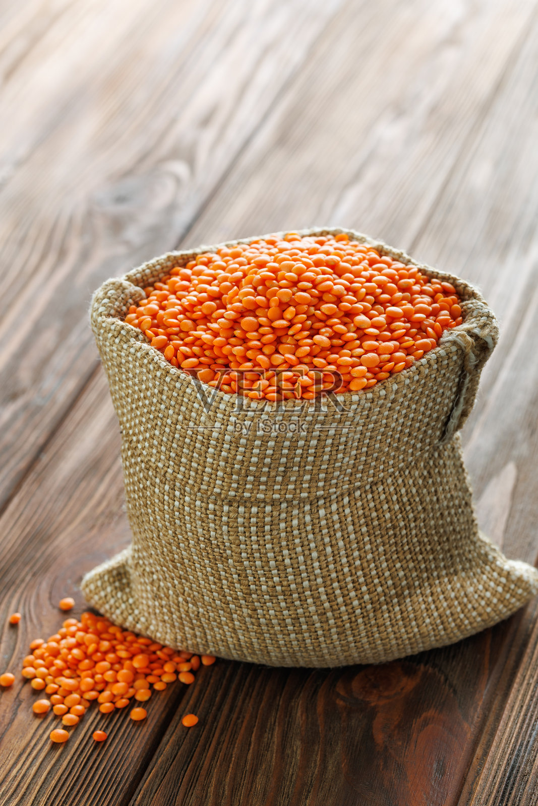 红扁豆从麻布袋中溢出，洒落在古朴的木桌上，营造出温暖而宜人的场景。照片摄影图片