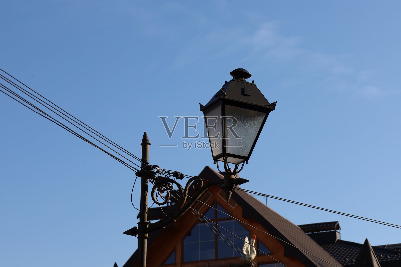 照片展示了一盏安装在建筑物屋顶上的街灯。灯具设计经典，金属主体和玻璃灯罩。灯体上可见字母L。灯的左侧有电线延伸，穿过天空。照片摄影图片