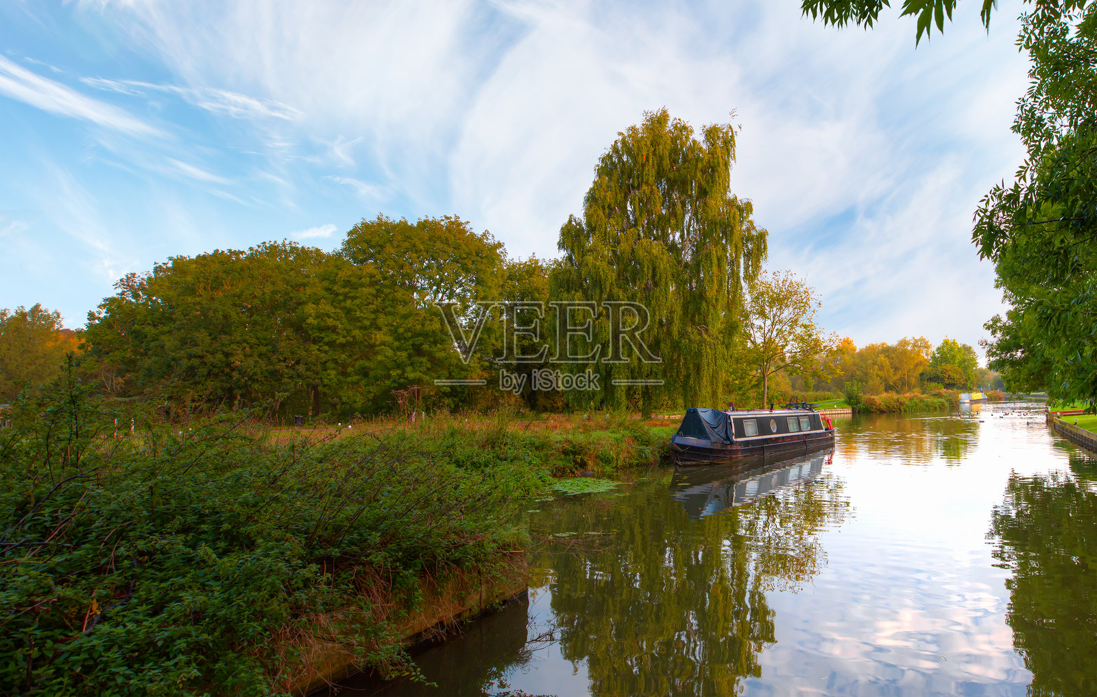 河中船只在绿色森林的庇护下，秋季森林的倒影映在水面上 - 英国伦敦的索布里奇沃斯特河照片摄影图片