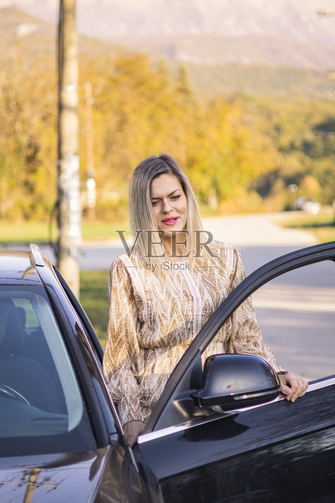 穿着裙子的金发女人在开车时休息。她正在享受日落，欣赏风景。自由的概念。照片摄影图片