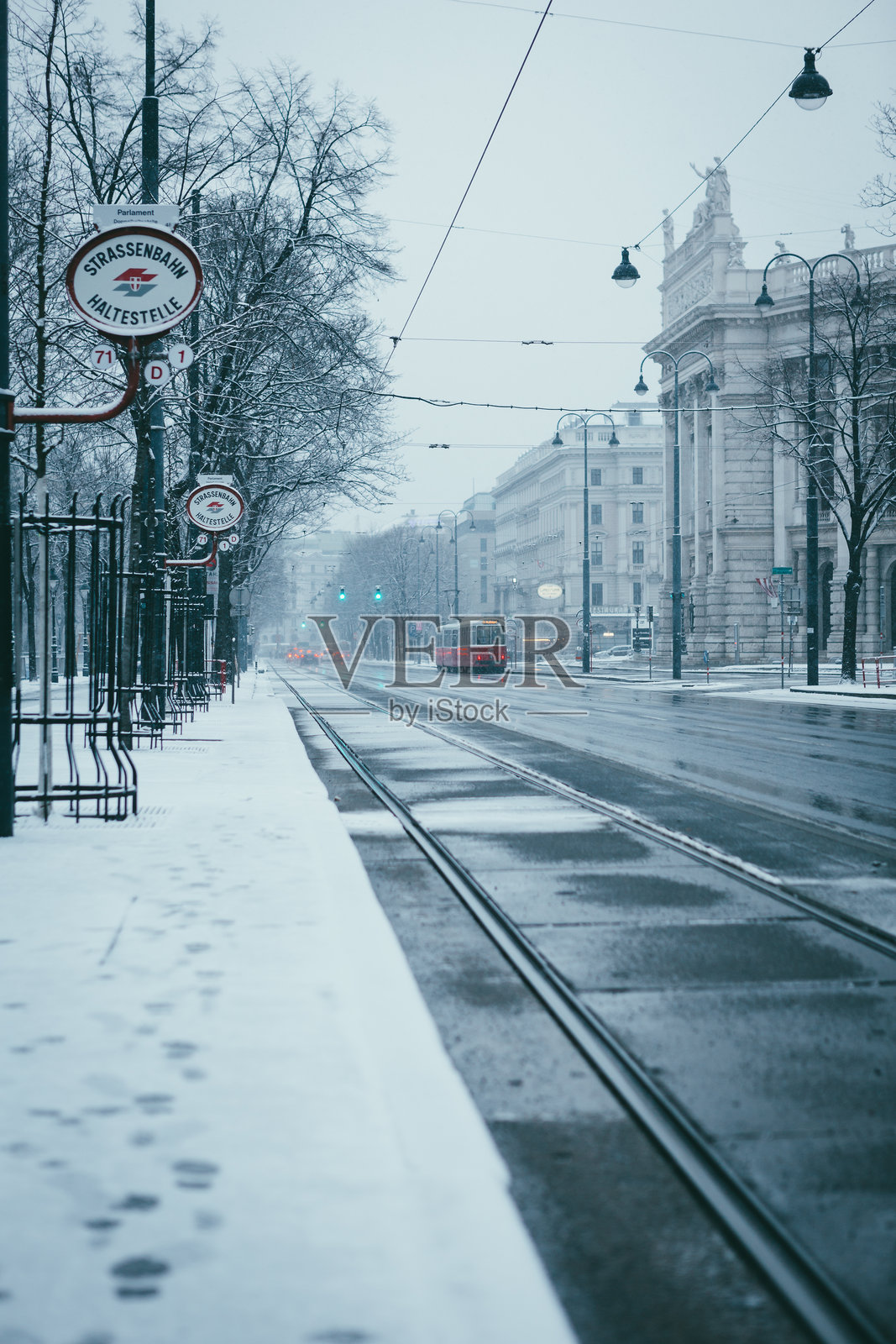 从电车站看雪覆盖的林荫大道，背景有剧院和复古交通。照片摄影图片