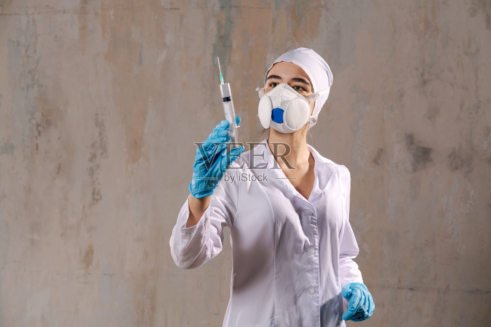 穿着白色实验室外套的女性手持注射器，佩戴口罩和手套。照片摄影图片