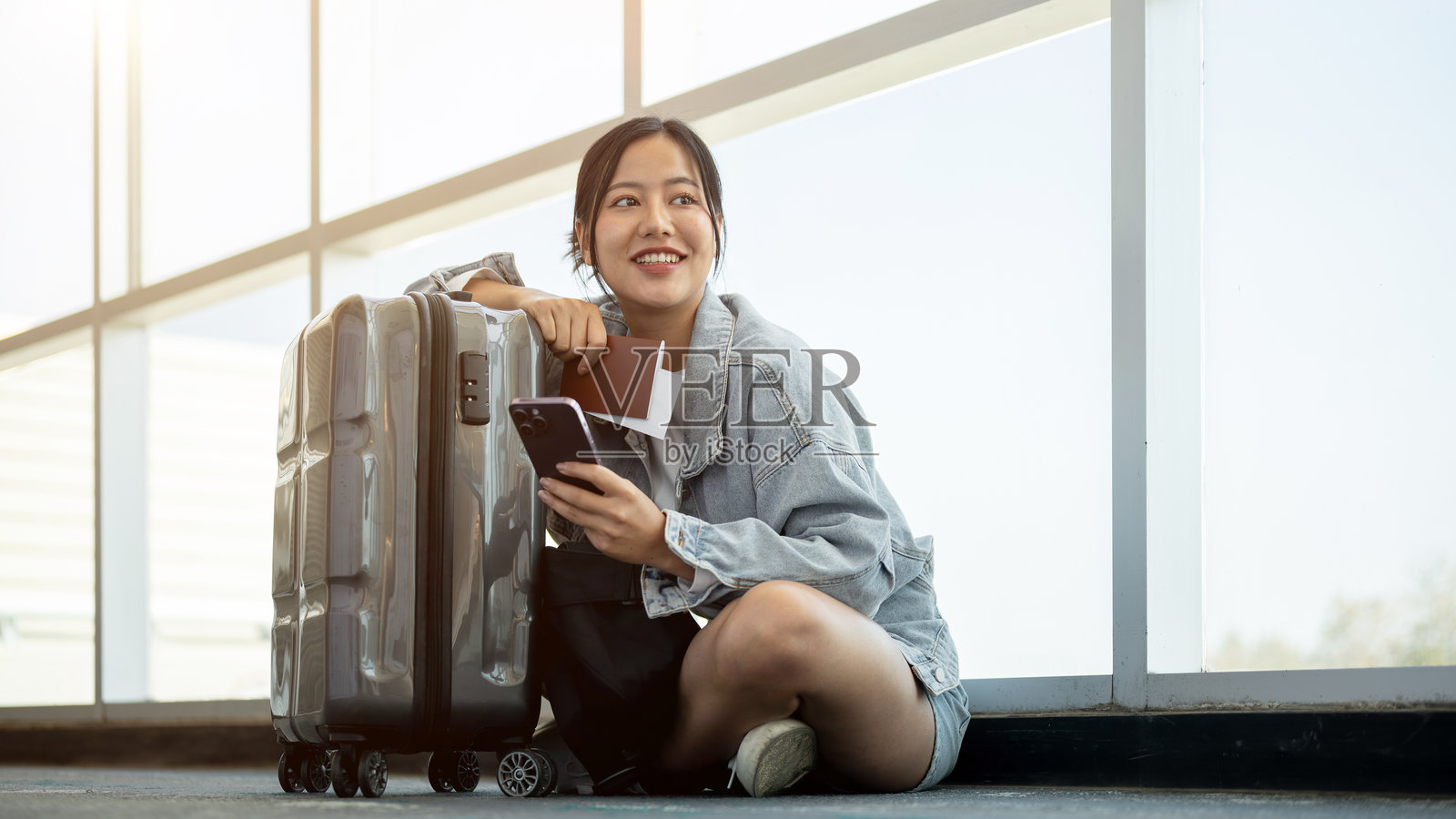 一位积极的亚洲女性乘客坐在机场候机厅的地板上，等待她的航班。照片摄影图片