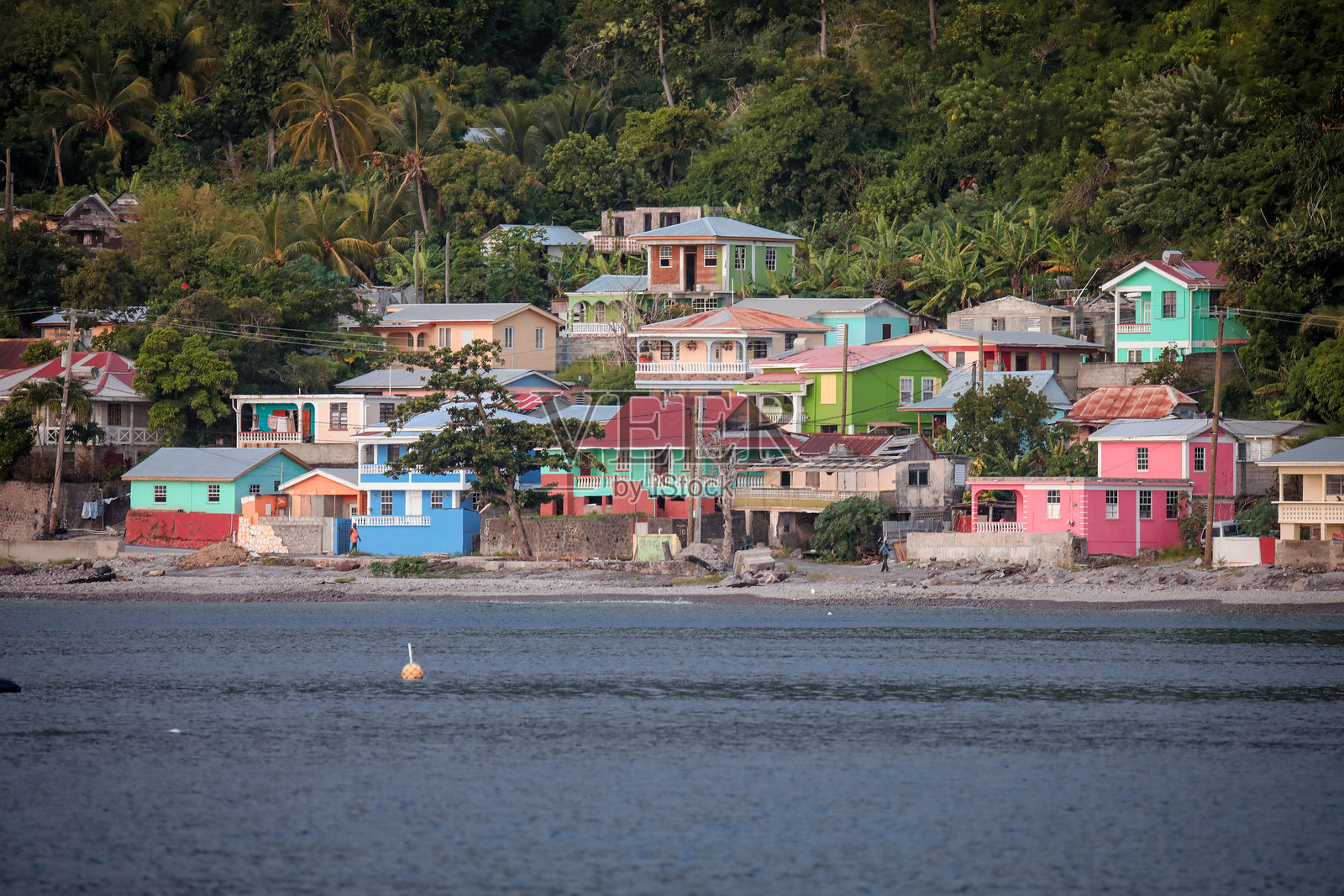 多米尼加岛的海岸边排列着五彩斑斓的房屋，背后是郁郁葱葱的山坡。照片摄影图片