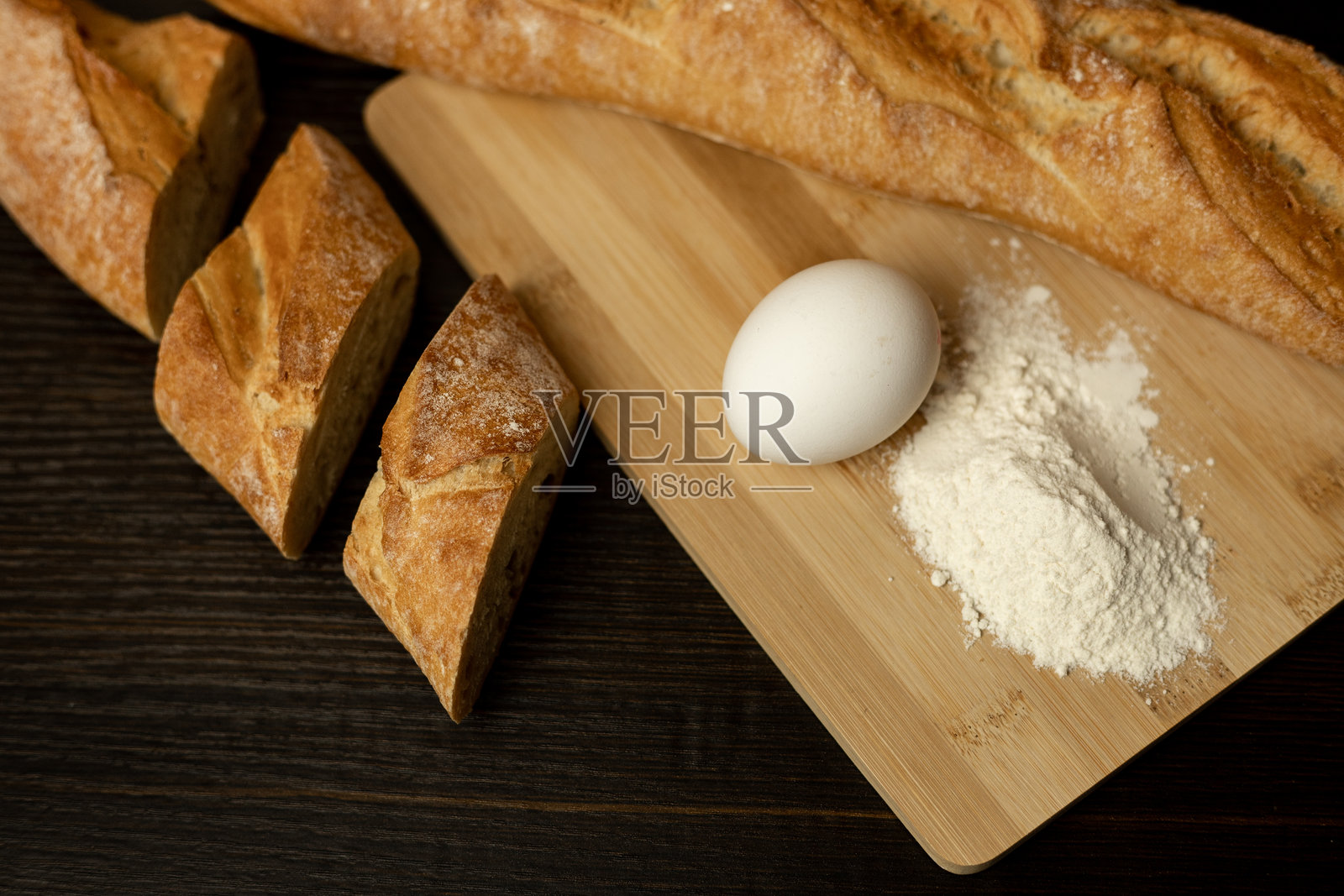 新鲜出炉的面包在陶土盘子里，桌子上有面粉、鸡蛋和面包。照片摄影图片