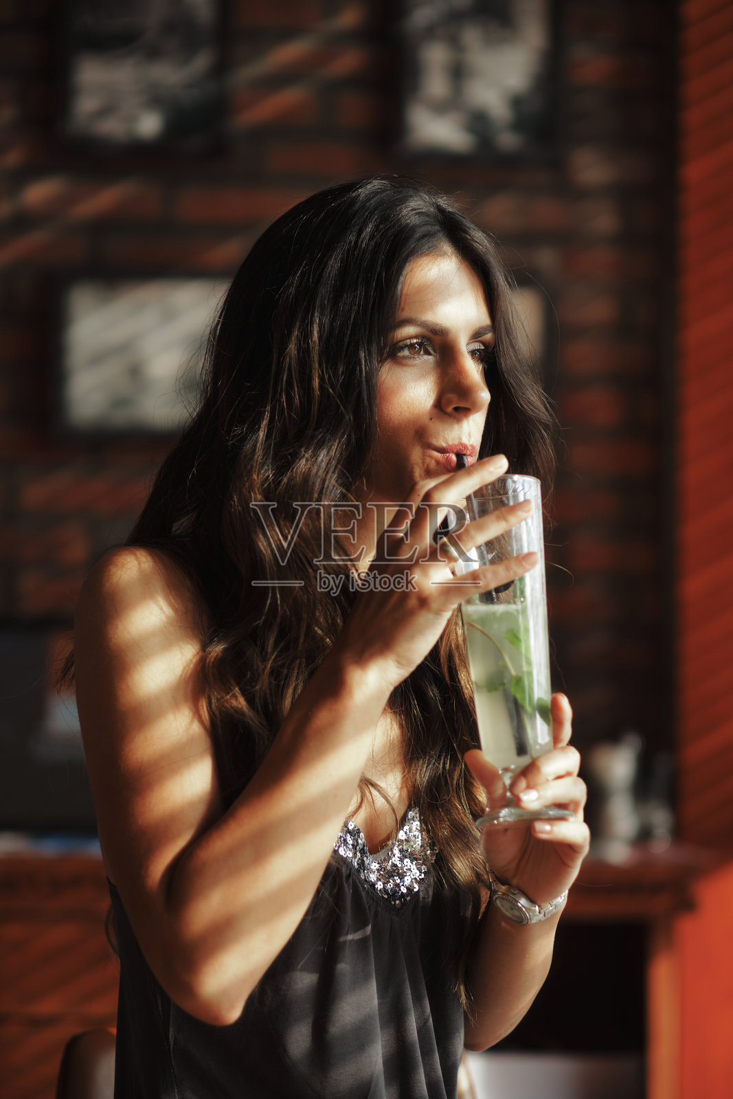 一位年轻美丽的黑发女性在咖啡馆里喝着莫吉托。照片摄影图片