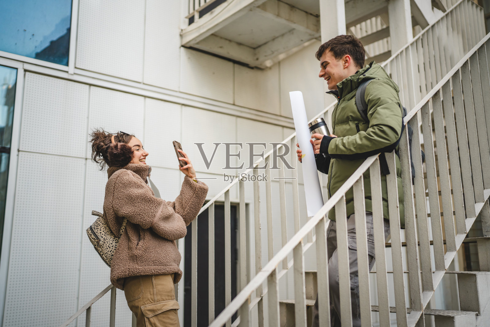 年轻女性在楼梯上用手机拍摄年轻男性的照片照片摄影图片