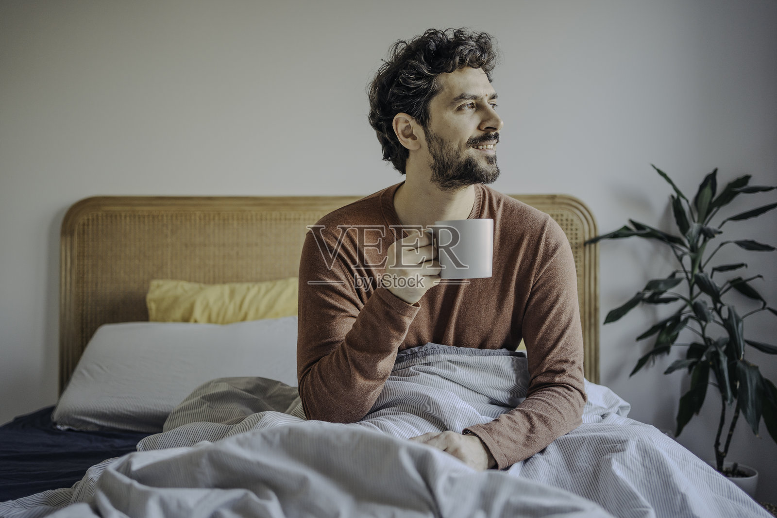 放松的年轻帅气中东男子在床上享受早晨咖啡。照片摄影图片