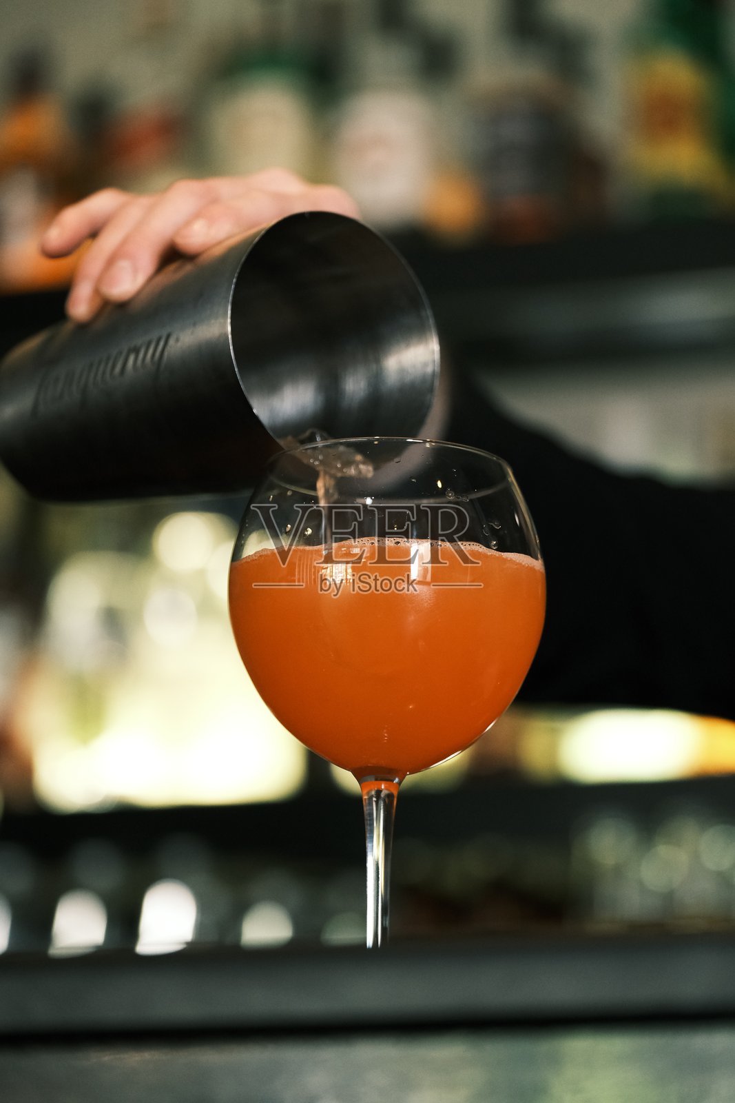 调酒师将橙色鸡尾酒倒入酒杯中，使用专业调酒器，在吧台上进行调酒和手工饮品准备，优雅酒具中的清爽酒精饮料。照片摄影图片
