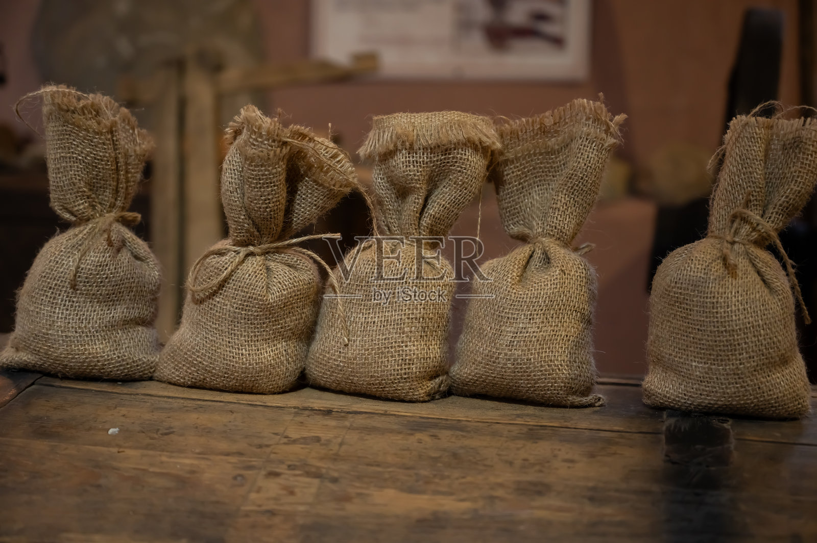 一排用麻绳绑好的小麻布袋，整齐地摆放在质朴的木质表面上，唤起一种复古农业、传统包装或有机储存的感觉。照片摄影图片