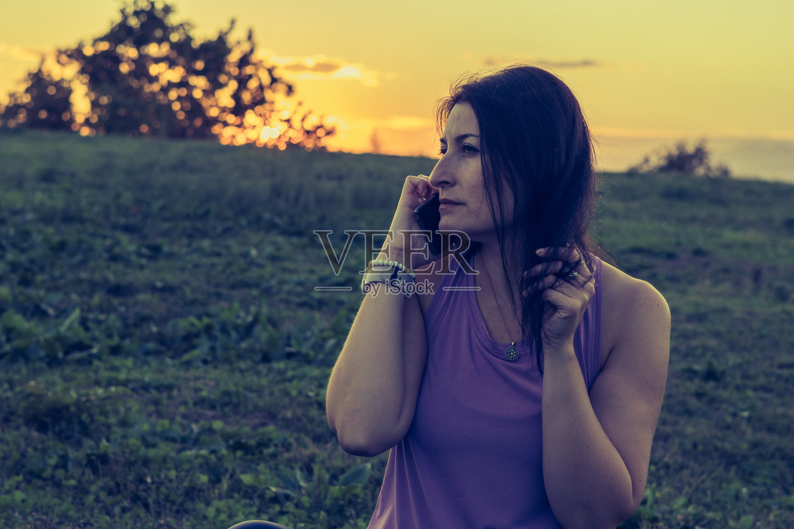 中年女性在日落或黄昏时分的自然环境中放松，正在用手机通话。照片摄影图片
