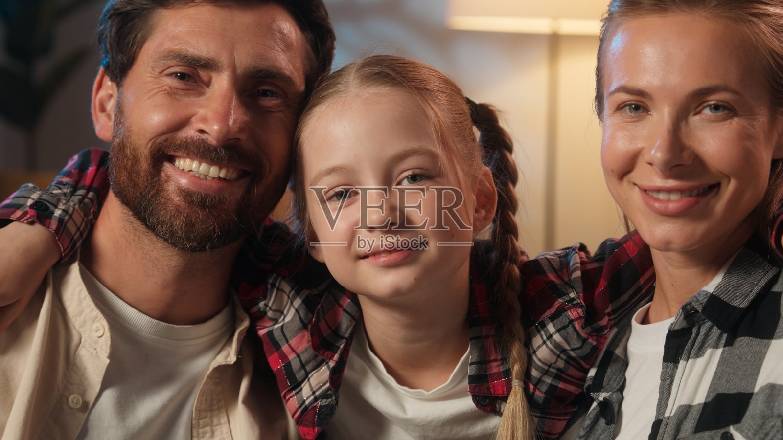 快乐的白人家庭在家中晚上的合影，毫无顾虑的父母，母亲和父亲亲吻小女儿的脸颊，孩子们在镜头前微笑，展现出爱与亲密的养育关系。照片摄影图片