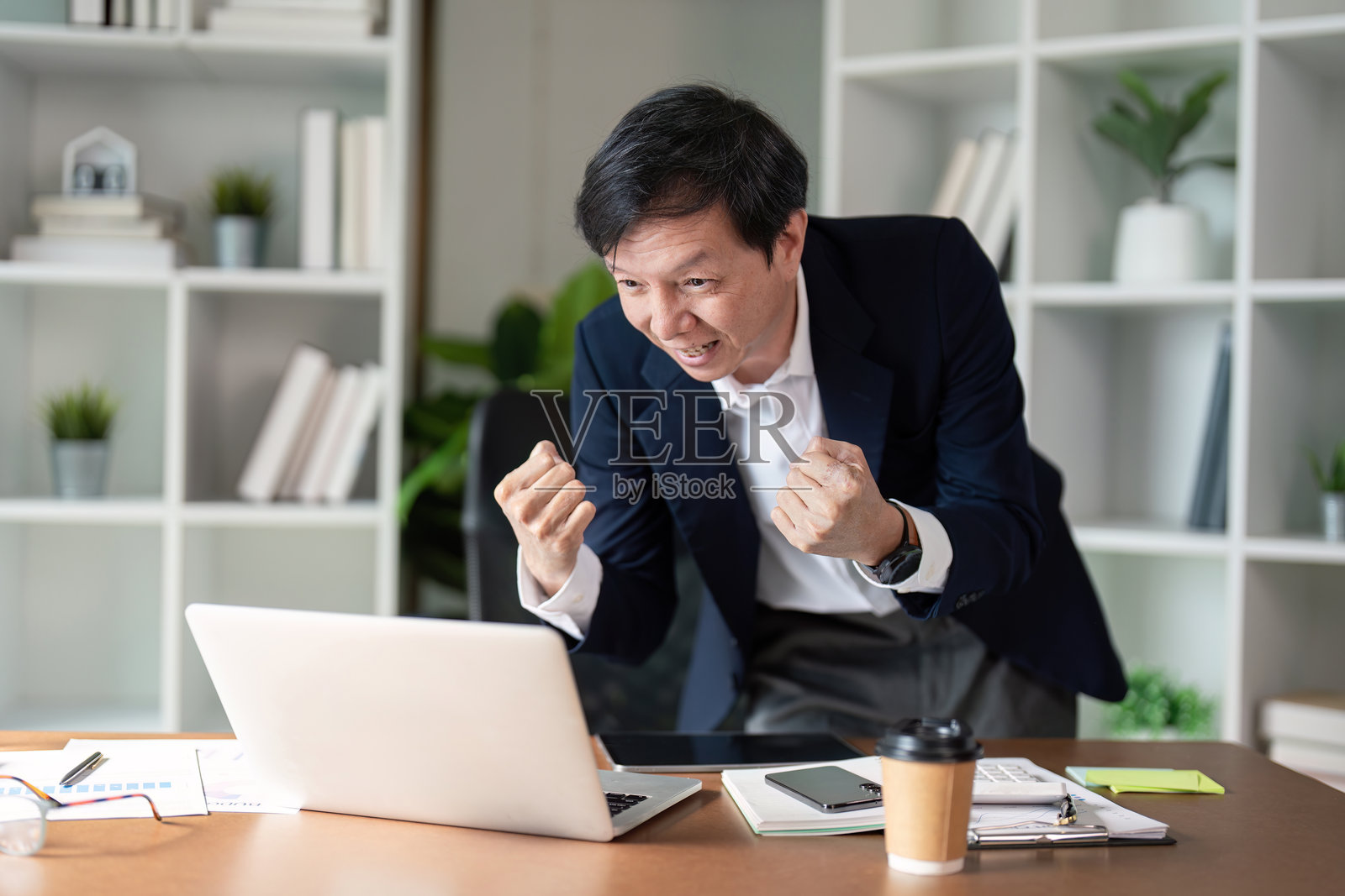 老年商人在现代办公室里使用笔记本电脑庆祝成功。照片摄影图片