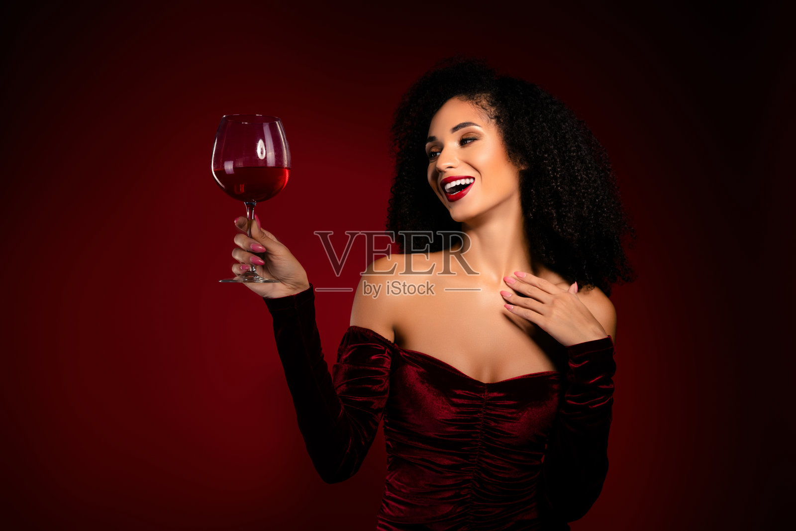 迷人的时尚女士微笑着，享受着一杯红色香槟，手触胸前，穿着节日盛装。照片摄影图片