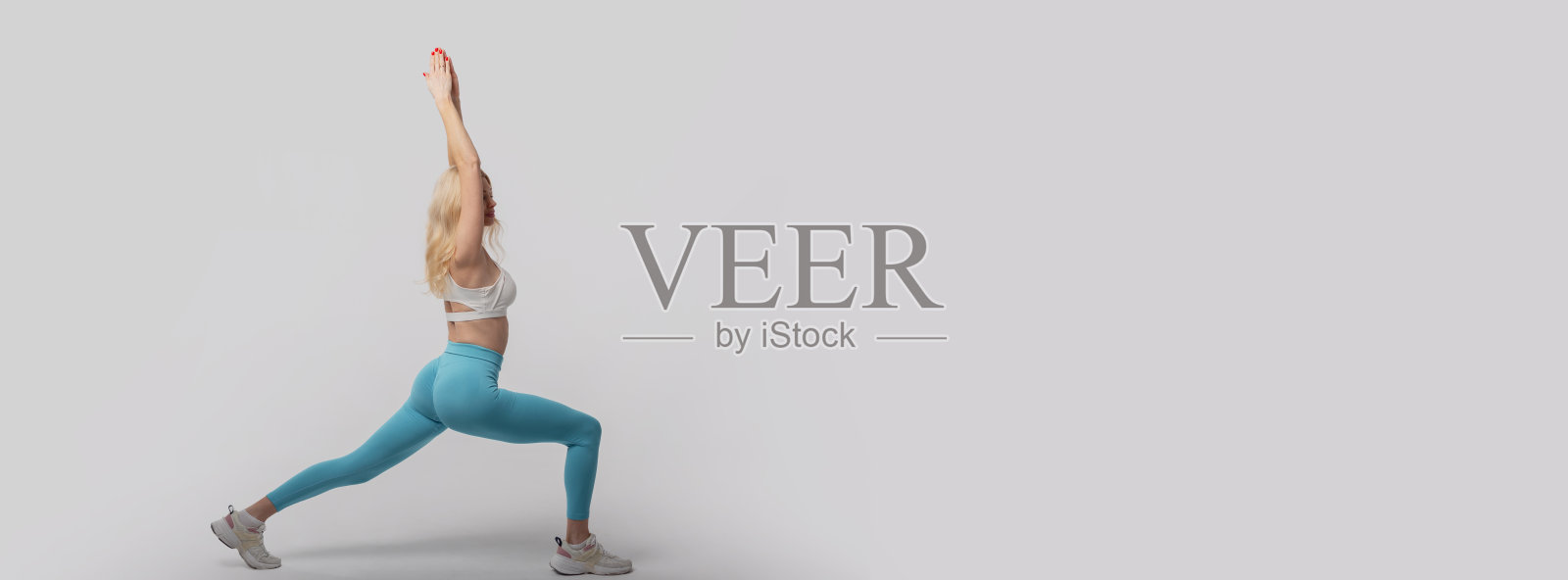 美丽苗条的年轻健身女士穿着运动服，在灰色背景的工作室里热身并拉伸腿部。漂亮的运动女性。文本和设计的自由空白空间。照片摄影图片