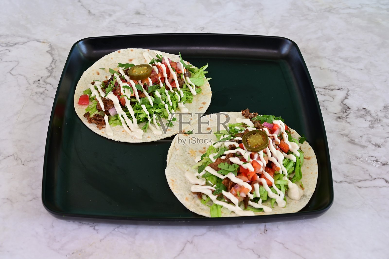 两只放在黑色盘子上的奶油酱塔可照片摄影图片