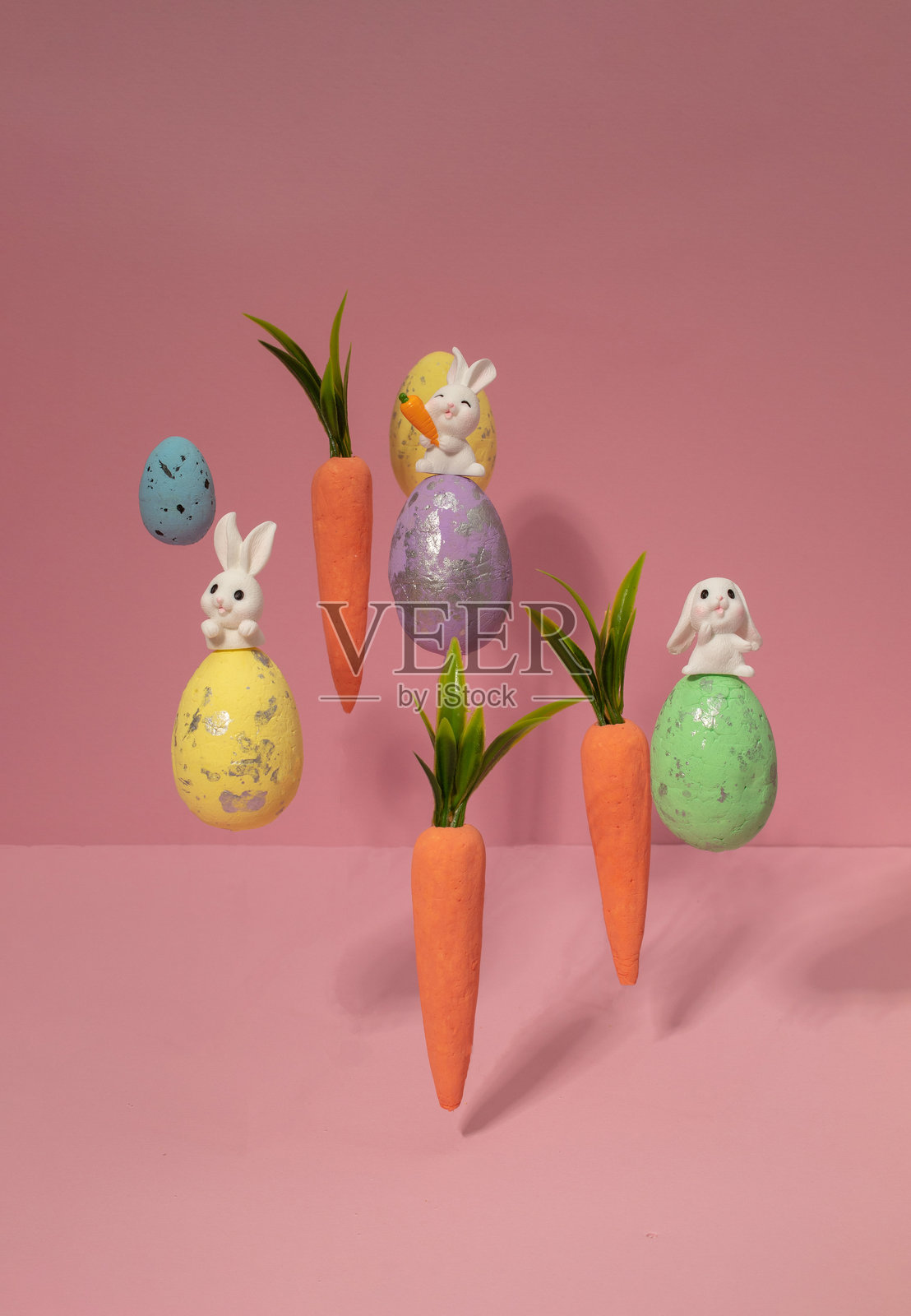 以胡萝卜、鸡蛋和兔子为主题的复活节布局，背景为柔和的粉色。创意简约的节日概念。平铺展示。照片摄影图片