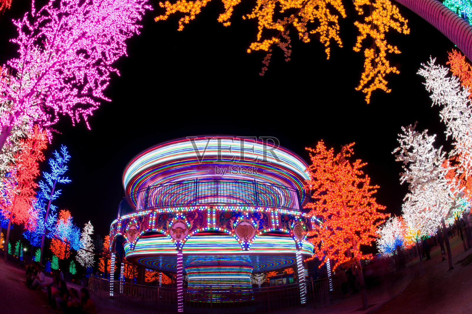 游乐园的秋千游乐设施。夜晚旋转的游乐设施，闪烁着明亮的紫色、红色、绿色和黄色灯光。照片摄影图片