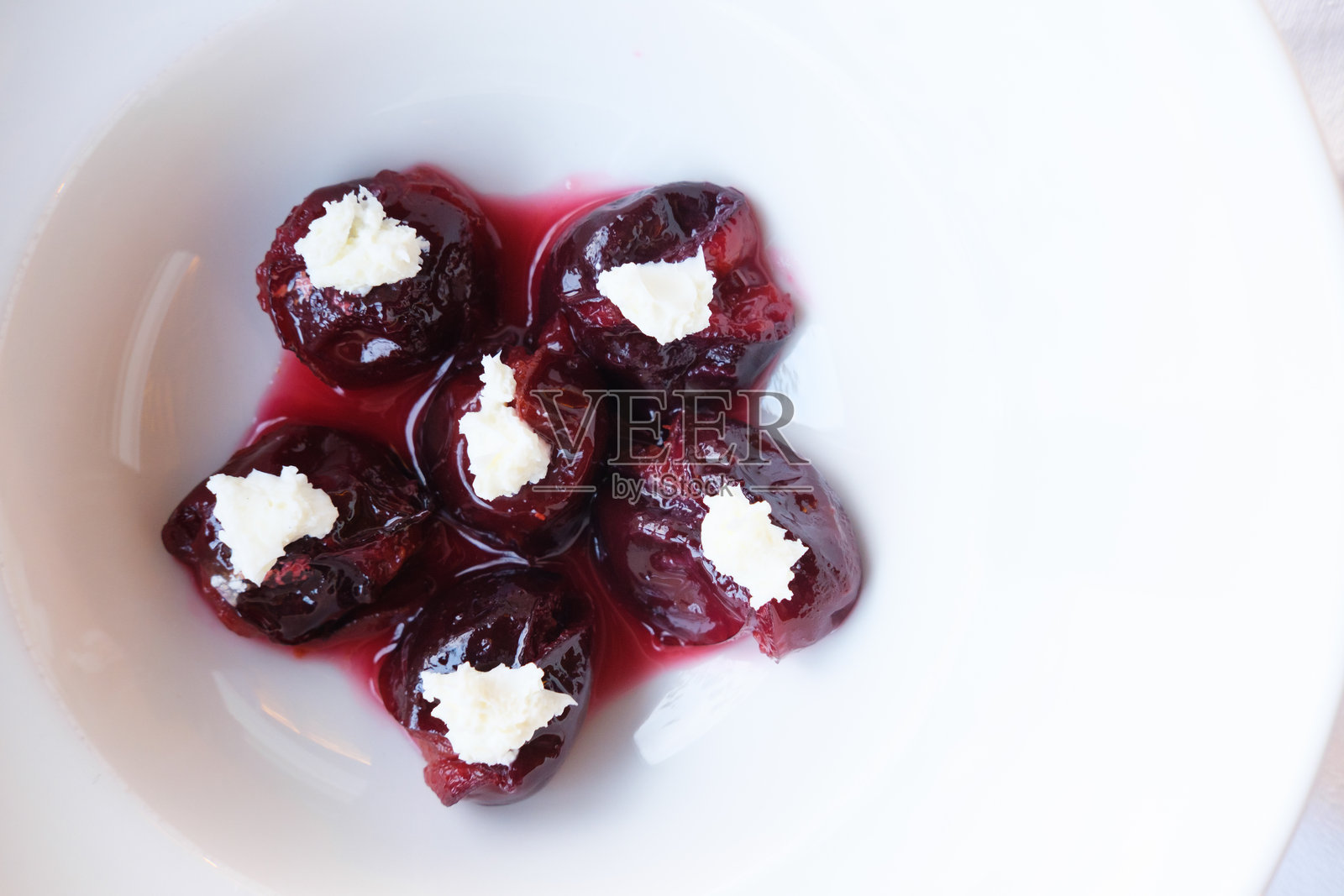 甜梅子浸泡在浓郁的糖浆中，上面放着一勺奶油奶酪照片摄影图片