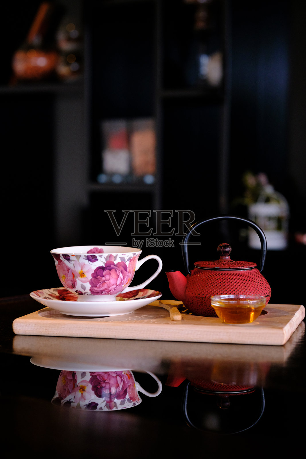 花卉茶杯和红色茶壶放在木板上，映照在黑色表面上照片摄影图片