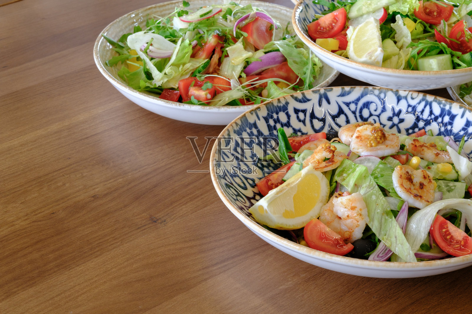 一张桌子上摆放着三种色彩鲜艳、清新的沙拉，每种沙拉都有独特的配料和调料。照片摄影图片