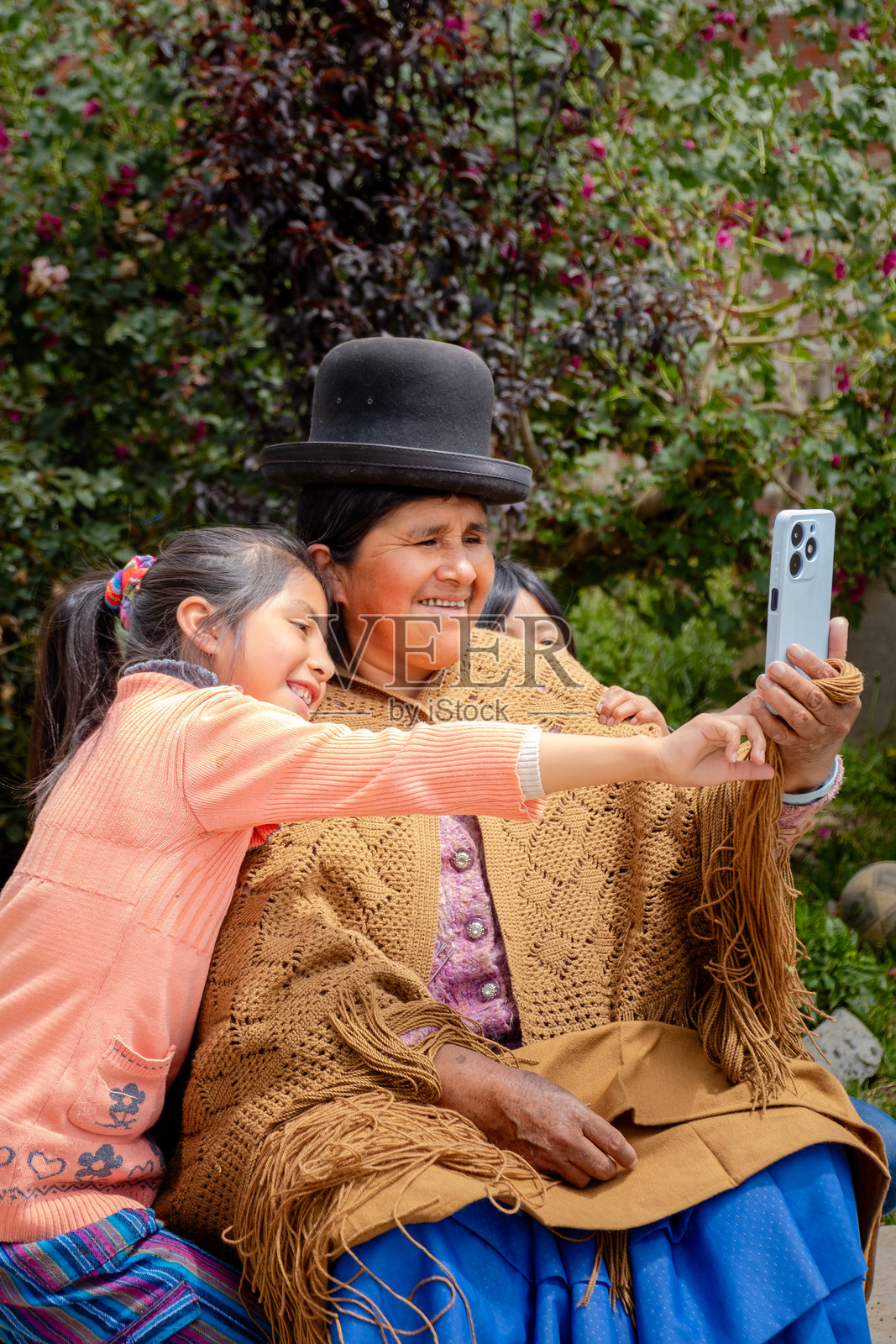 身穿波列拉裙的阿伊马拉祖母在拉巴斯市的家院子里与两个孙女一起用手机自拍 - 交流概念照片摄影图片