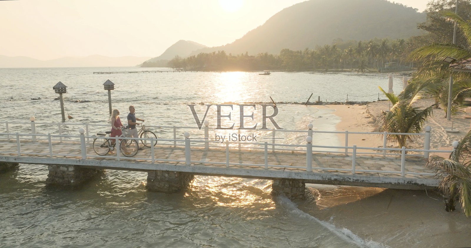 日出时分，情侣在码头上骑自行车散步的鸟瞰图照片摄影图片