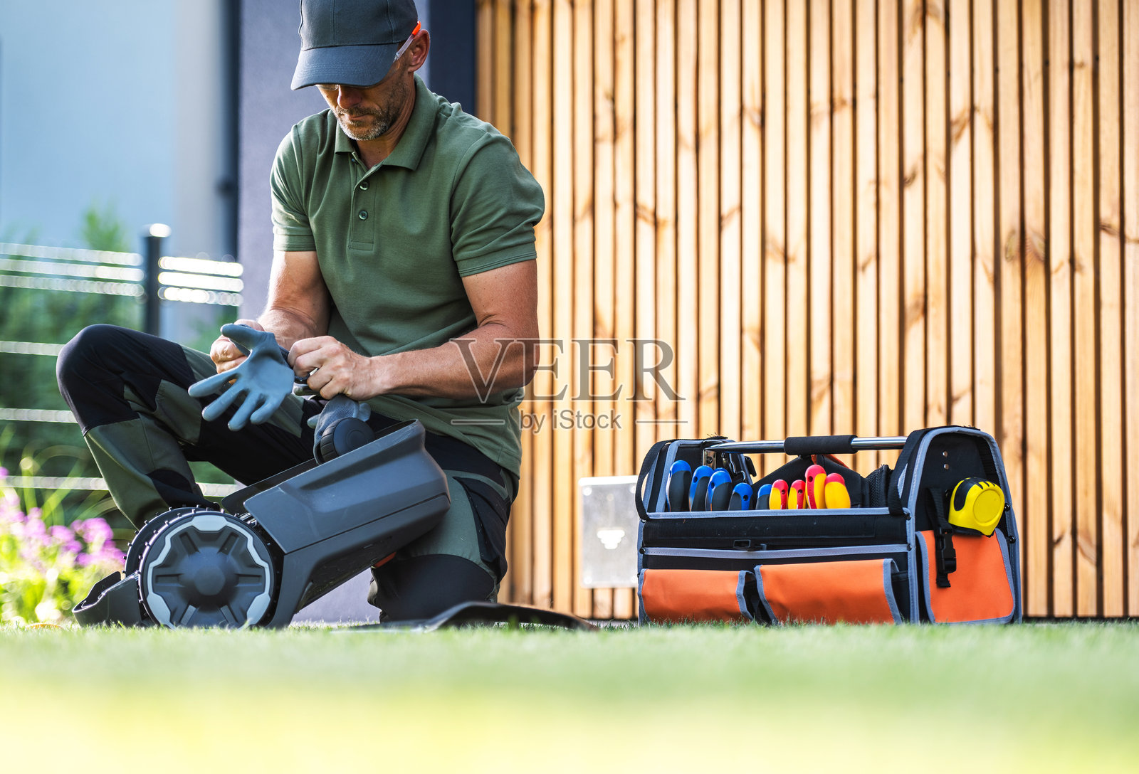 男人在阳光明媚的日子里准备园艺工具，靠近木栅栏和五彩缤纷的花朵。照片摄影图片