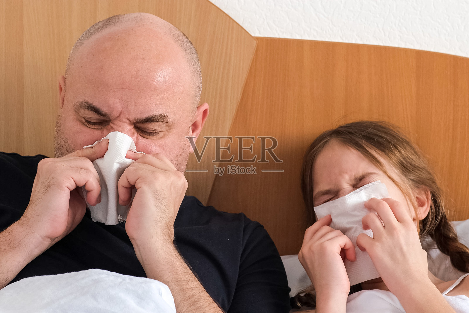 一家人，父亲和女儿躺在床上用纸巾擤鼻涕照片摄影图片
