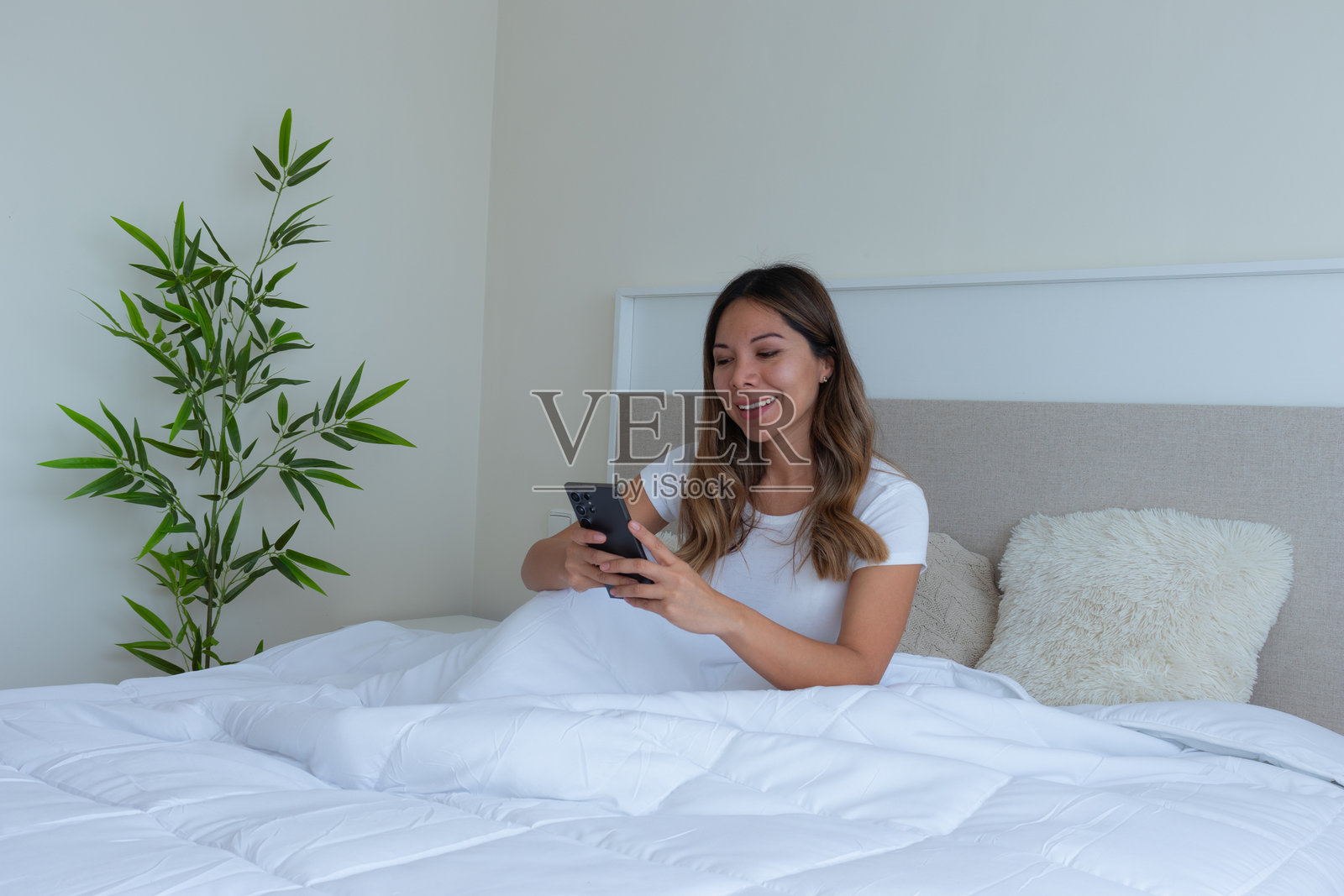 卧室里白色床上的女人与手机照片摄影图片