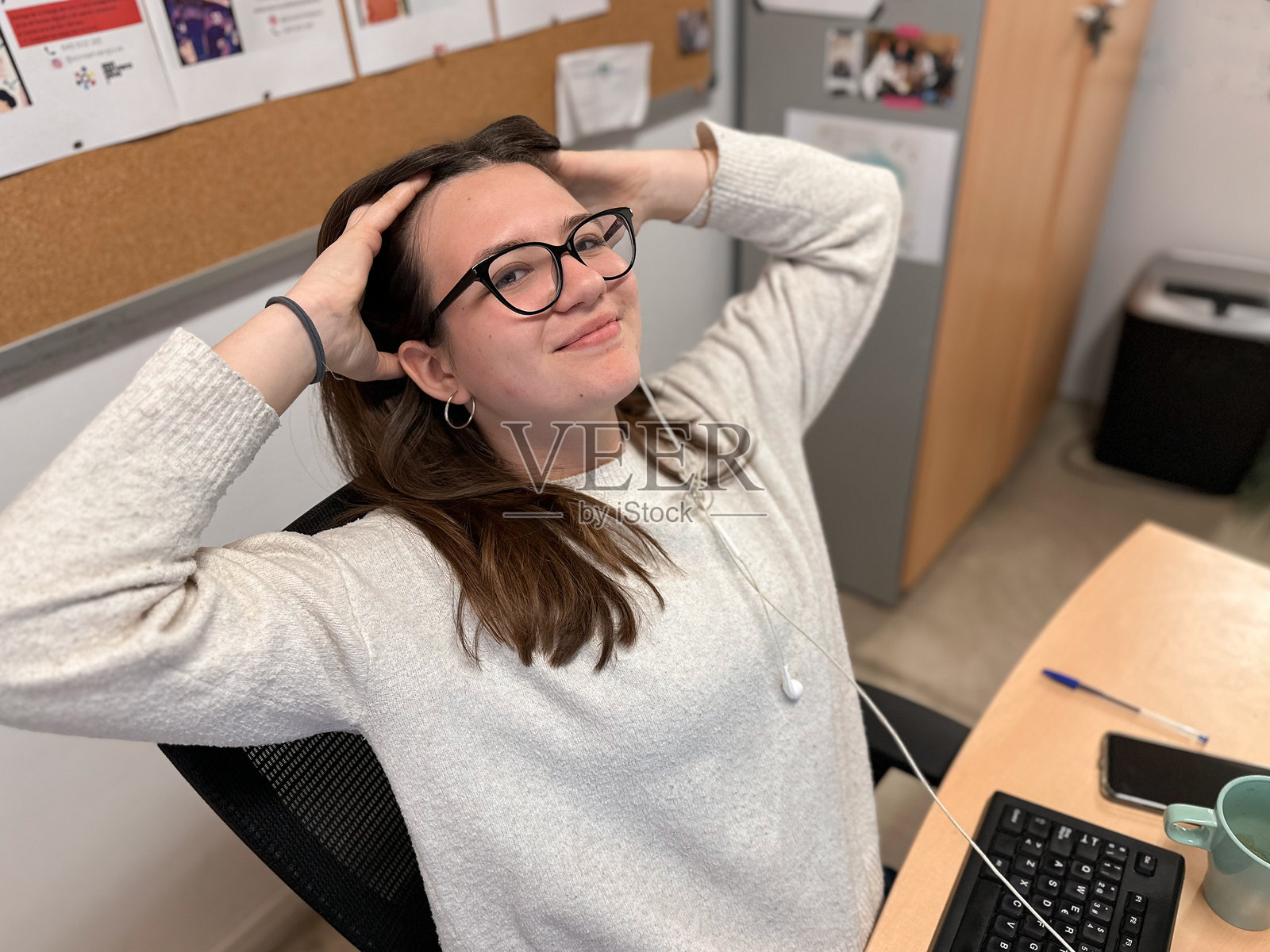 微笑的青少年女学生坐在桌子前，看着镜头，在电子学习休息期间做背部和头部拉伸。照片摄影图片