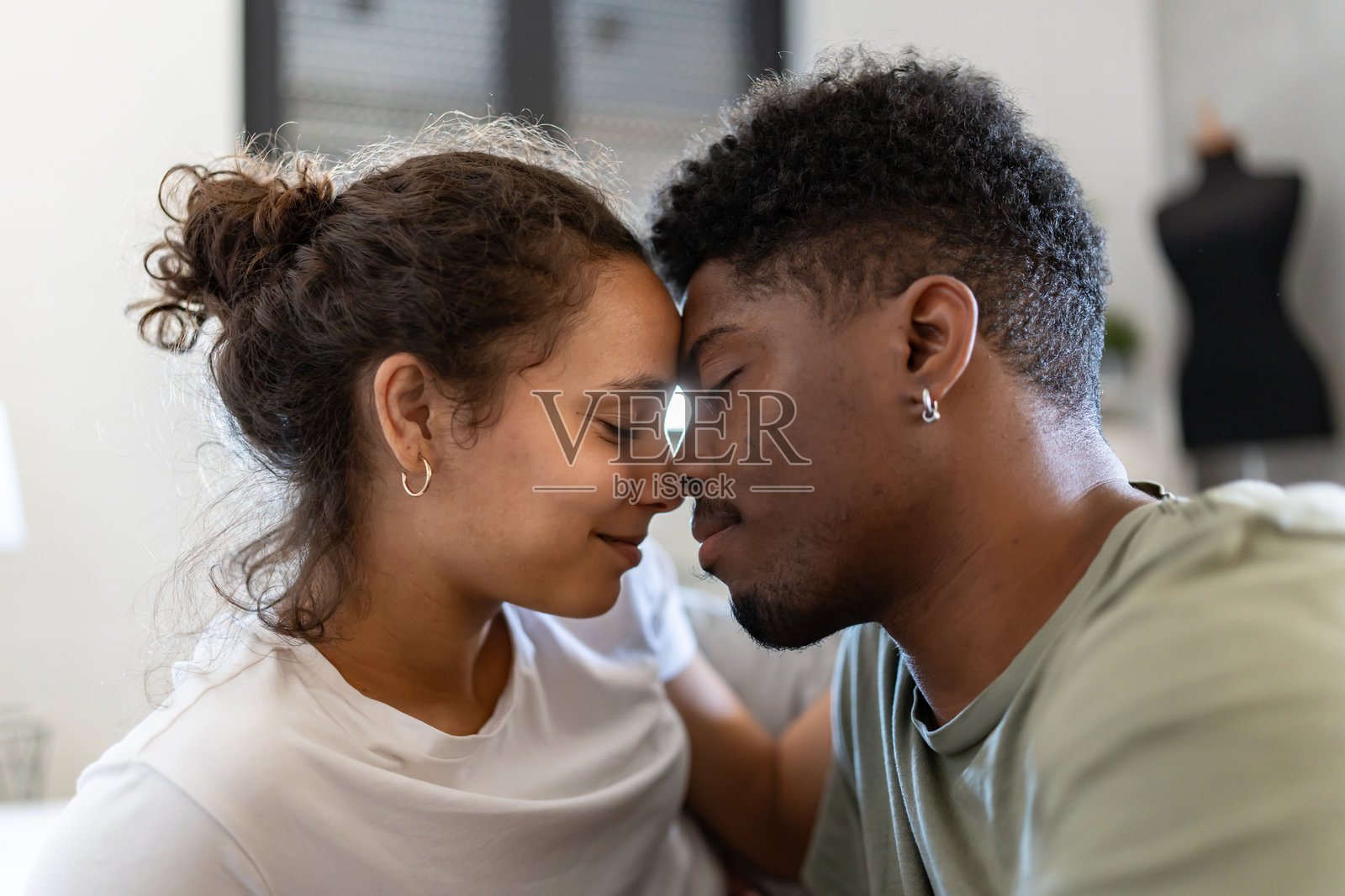 一对恩爱情侣的特写，他们的额头相靠，闭着眼睛，在柔和的灯光下分享亲密而温柔的时刻。照片摄影图片