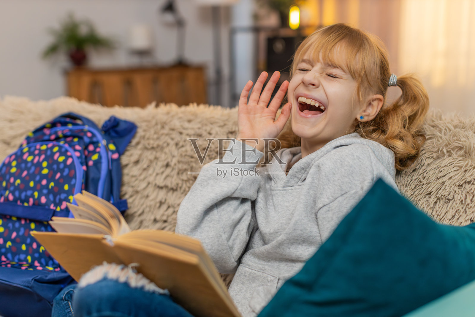年轻女孩坐在家里的沙发上阅读故事书，停下来欣赏插图，脸上露出温柔的微笑。照片摄影图片