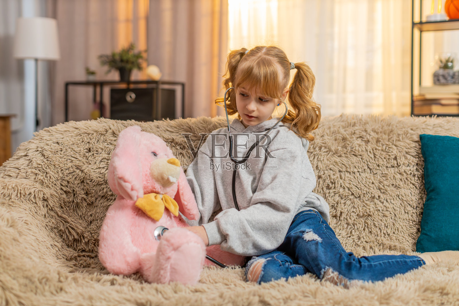 少女医生在家里的沙发上拿着玩具听诊器，温柔地询问小兔子哪里疼。照片摄影图片