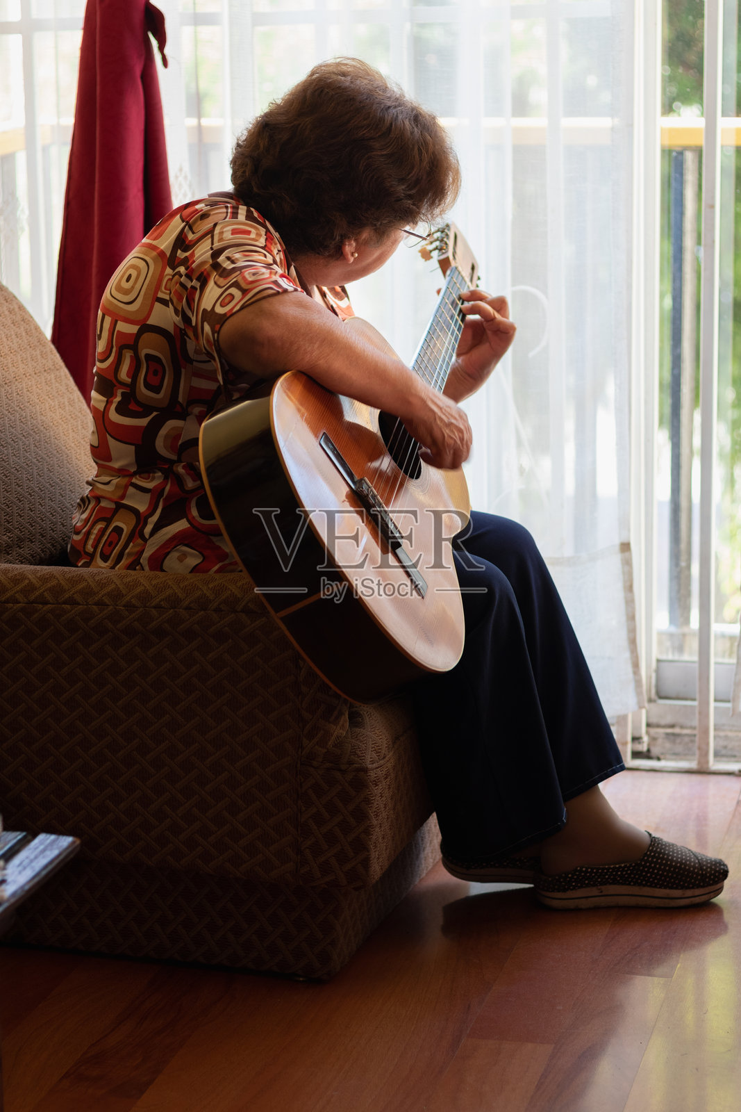 一位年长的拉丁裔女性坐着唱歌并练习吉他照片摄影图片