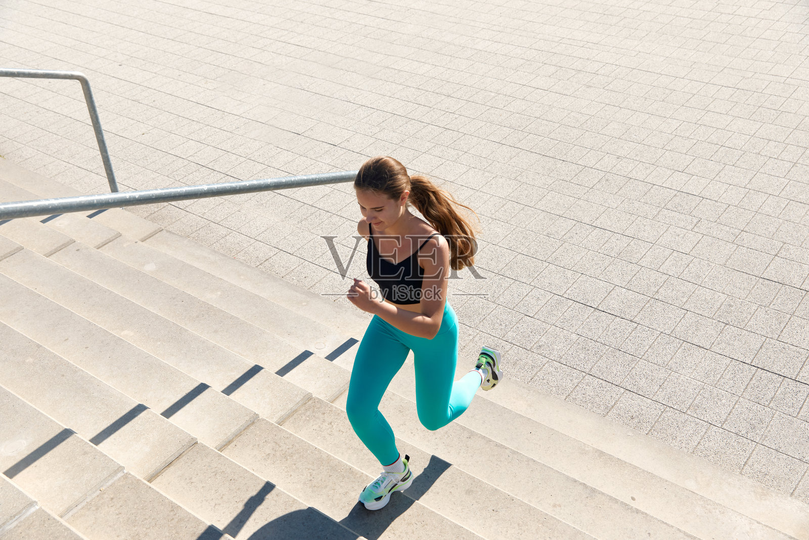 运动女性在城市中跑向石阶，佩戴无线耳机并使用健身追踪器照片摄影图片