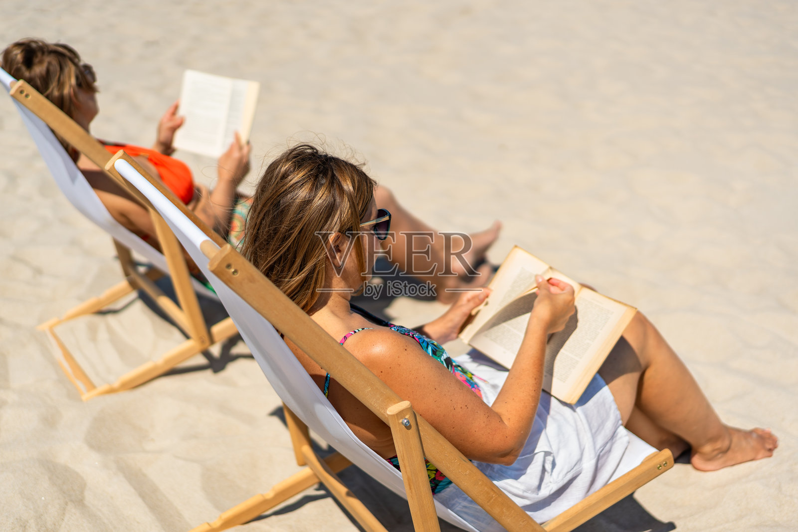 两位成熟的女性坐在沙滩椅上阅读书籍照片摄影图片