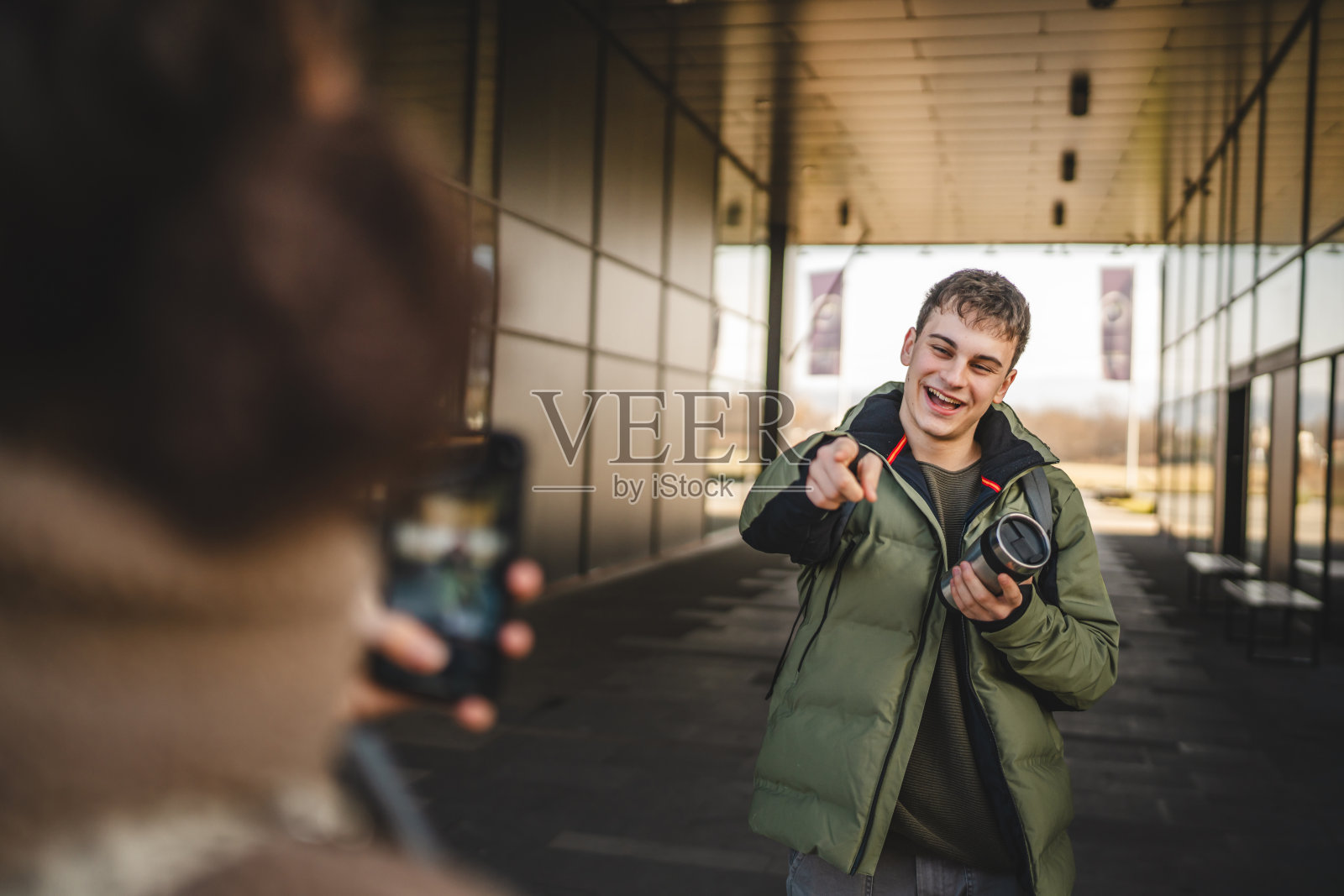 年轻男子手持保温杯，年轻女子正在给他拍照。照片摄影图片