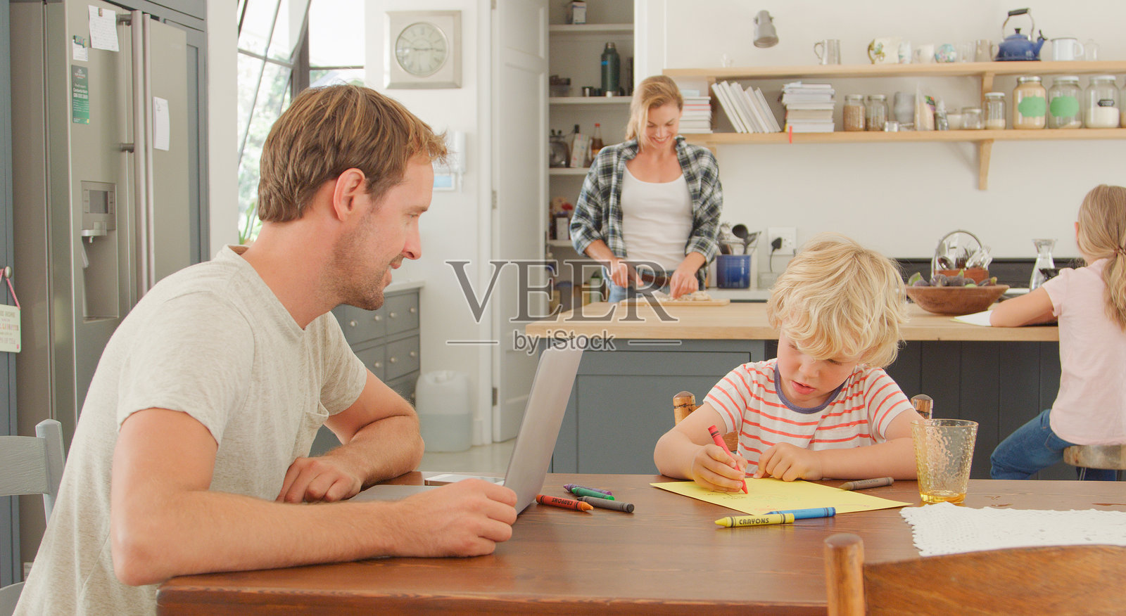 家庭在厨房，儿子在画画，父亲在使用笔记本电脑工作。照片摄影图片