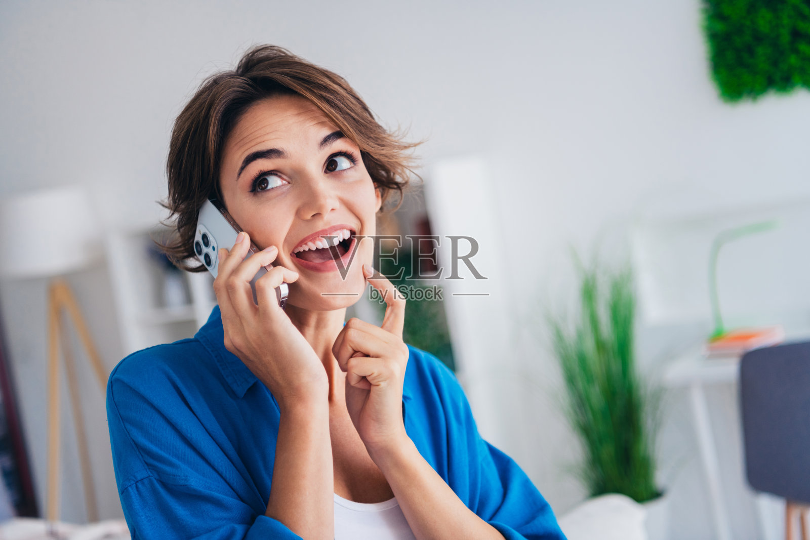 愉快的女士在公寓内闲暇时光中，手指轻触下巴，愉快地用电话交谈。照片摄影图片