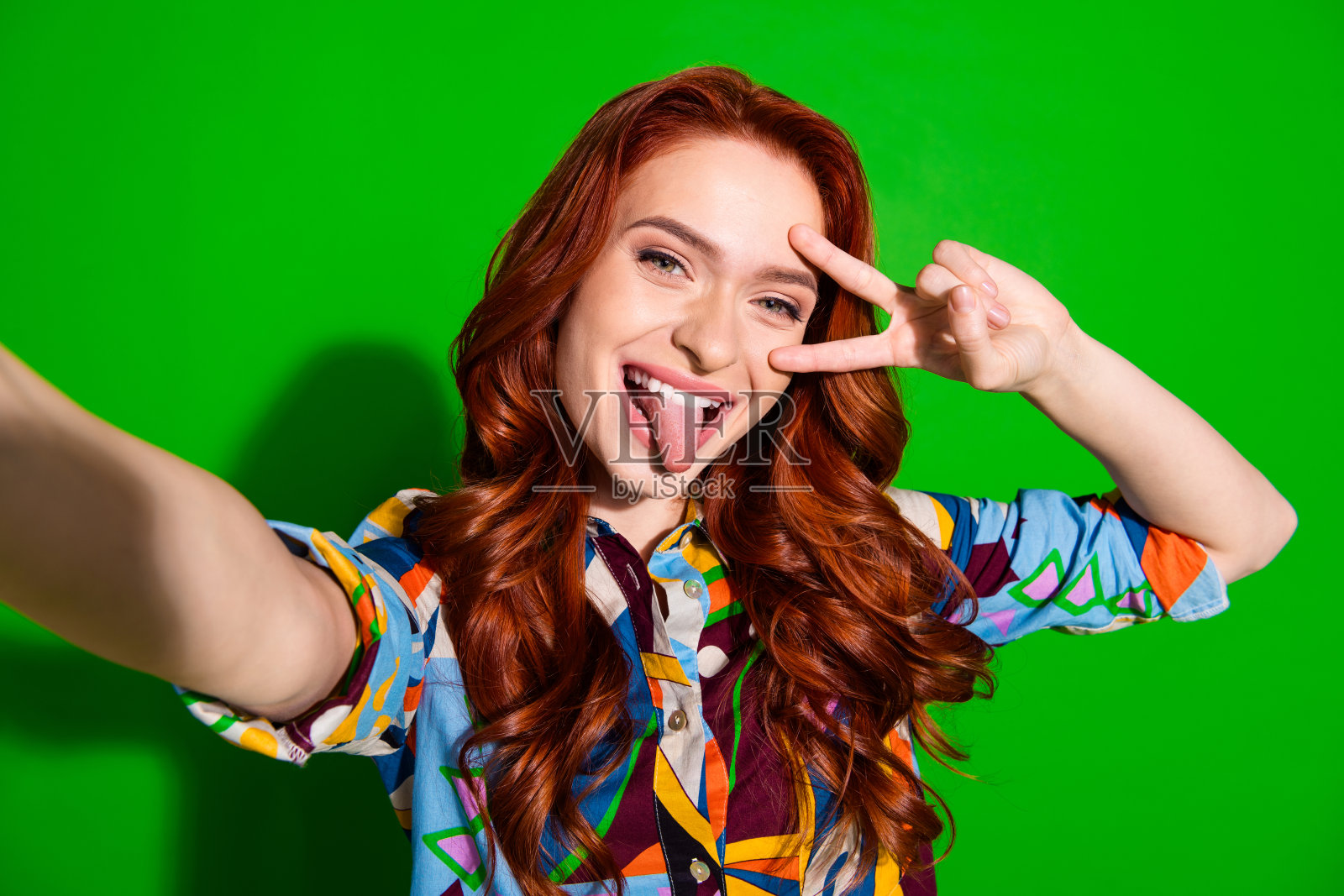 在绿色背景下做出和平手势的活泼年轻红发女性照片摄影图片