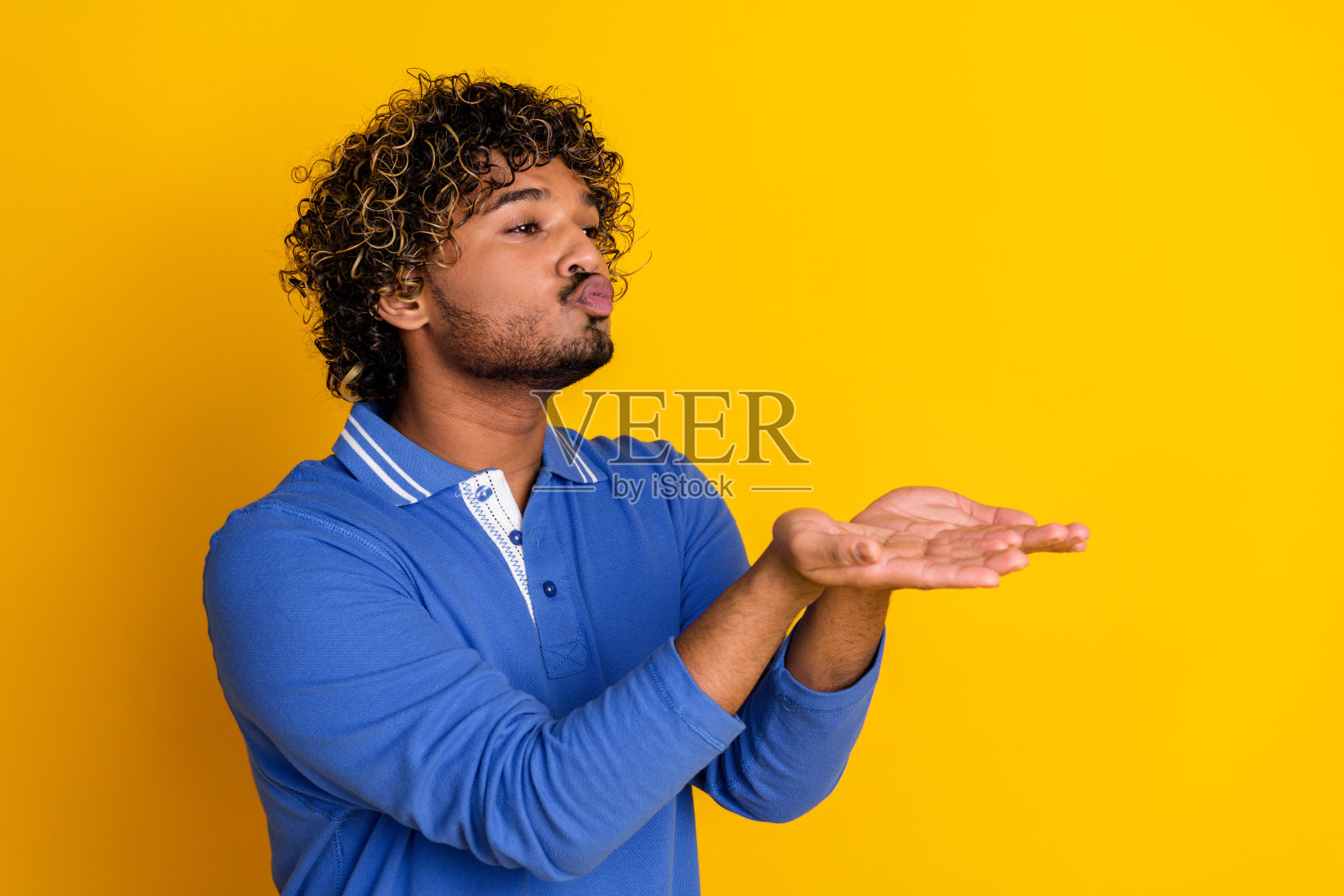 一位年轻男子在黄色背景下用手势表演，穿着蓝色休闲服装。照片摄影图片