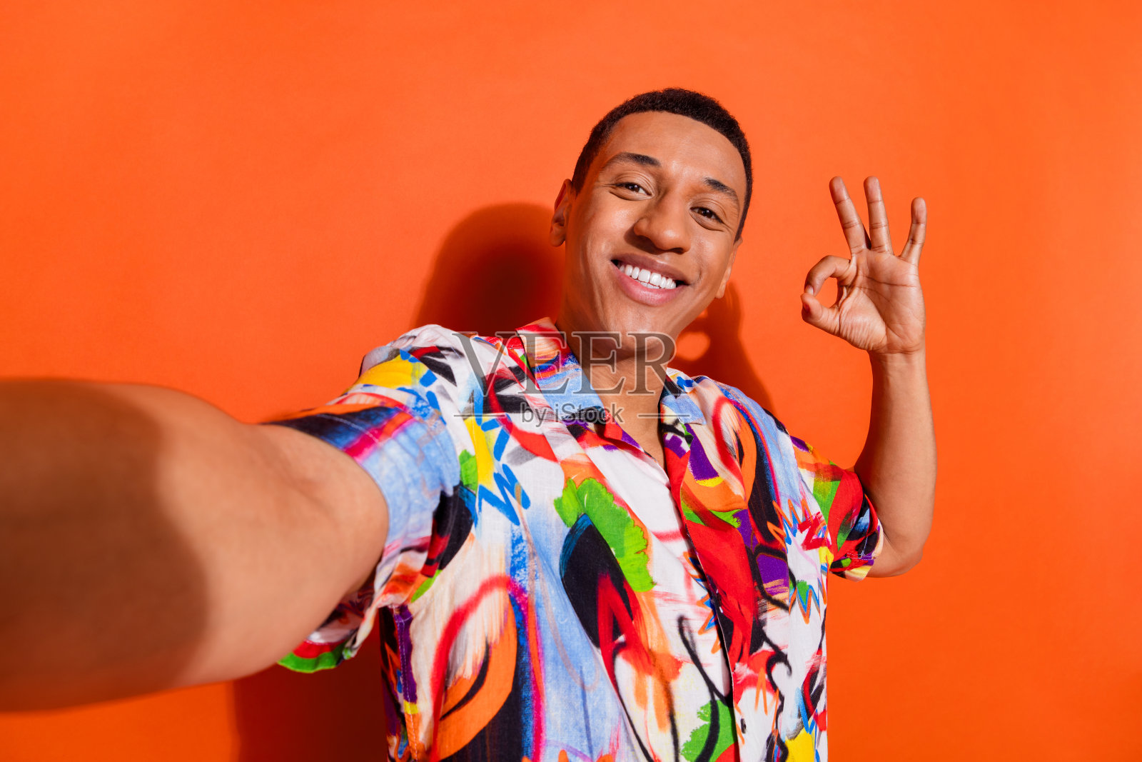 穿着色彩鲜艳印花衬衫的快乐年轻人，背景为生动的橙色，做出积极的手势，体现时尚和生活方式元素照片摄影图片
