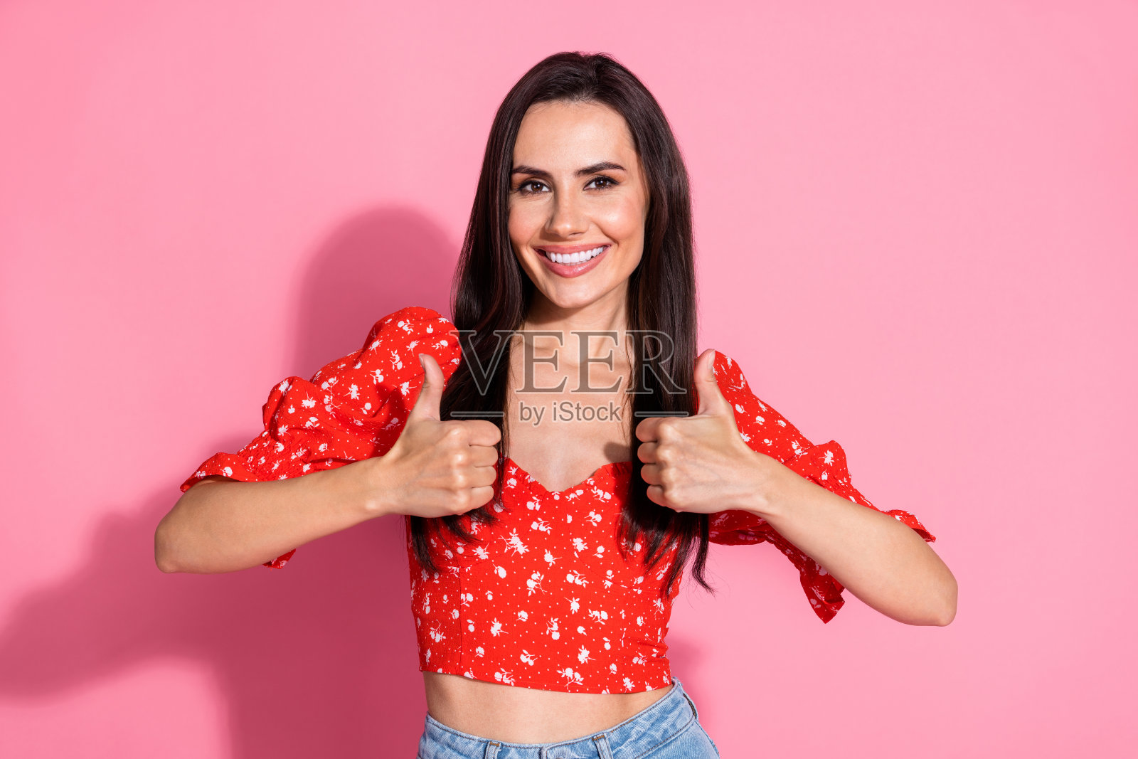 穿着复古红色上衣的微笑美丽年轻女性在粉色背景前竖起大拇指的肖像照片照片摄影图片